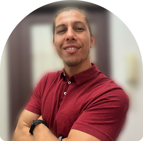 Chilean physiotherapist smiling confidently in a red polo shirt, promoting wellness and rehabilitation at Wellness on Shore.