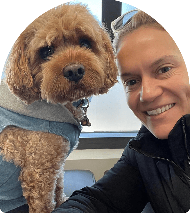 Woman smiling with a dog in a blue sweater, showcasing a friendly atmosphere and connection, reflecting the community spirit of Wellness on Shore.