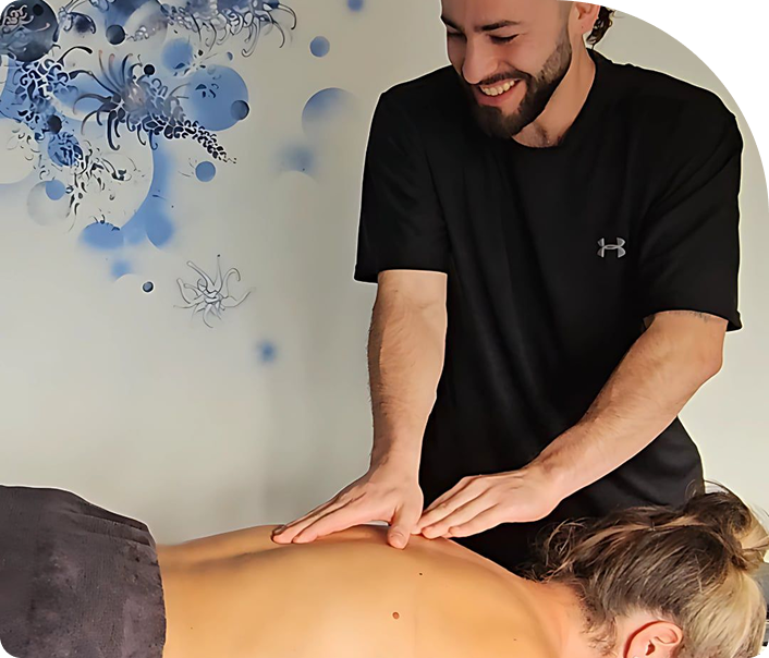 Remedial massage therapy session at Wellness On Shore, featuring a therapist applying hands-on treatment to a client's back, with a calming blue-themed wall design in the background.