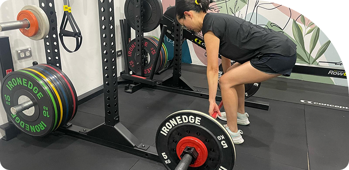 Woman performing deadlift with weights in a gym setting, showcasing personal training and fitness support at Wellness On Shore.