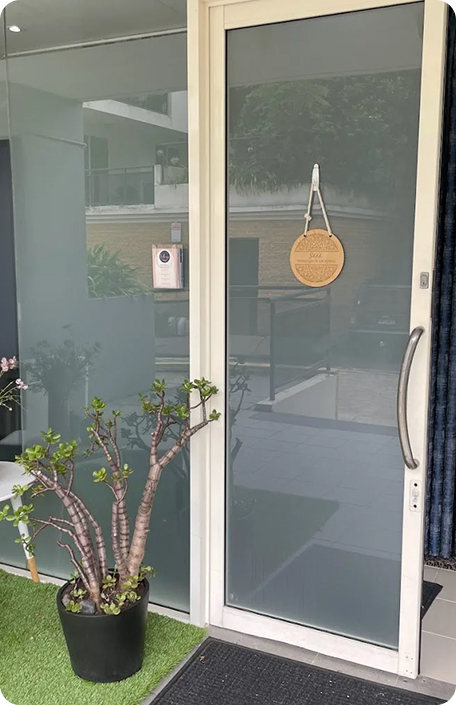 Glass door entrance to Wellness on Shore, featuring a decorative wooden sign and a potted plant, inviting visitors to the wellness center.