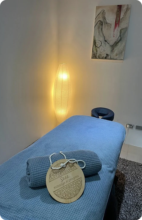 Massage treatment room at Wellness on Shore featuring a blue massage table, decorative lamp, and a sign reading "Shala massage in progress."