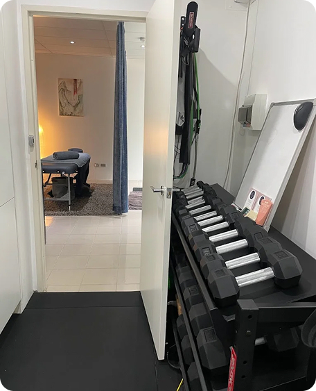 Treatment room and gym space at Wellness on Shore, featuring dumbbells, massage table, and serene lighting.