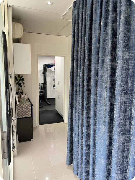 Interior view of Wellness on Shore, featuring a blue curtain, treatment area, and gym equipment in the background.