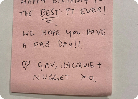 Happy birthday note on pink sticky paper expressing appreciation for a personal trainer, signed by Gav, Jacquie, and Nugget.