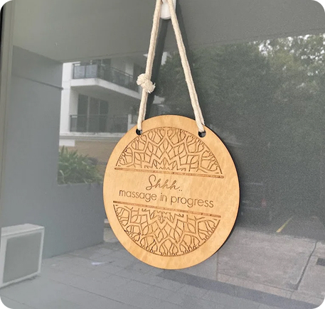 Wooden sign reading "Shhh... massage in progress," hanging outside a treatment room at Wellness on Shore, indicating a serene environment for wellness services.