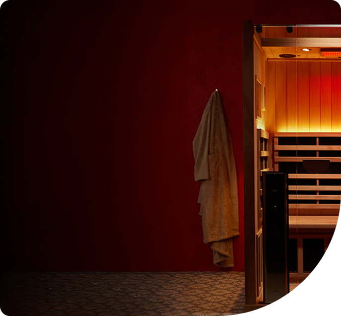 Infrared sauna with warm lighting, towel hanging on the wall, and calming red backdrop, promoting relaxation and detoxification at Wellness on Darling.