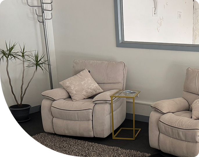 Reclining recovery chairs in a wellness center, designed for deep relaxation and comfort, featuring plush upholstery and decorative pillows, with a small side table and potted plant nearby.