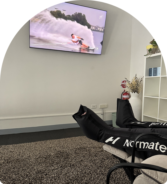 Recovery room at Wellness on Darling featuring Normatec compression boots, reclined seating, and a TV for relaxation, in a soothing environment designed for body restoration.