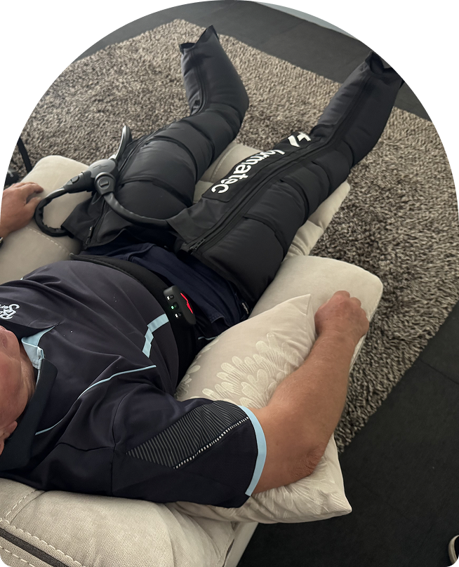 Person using Normatec compression therapy boots in a recovery room, relaxing on a sofa with a calming environment.