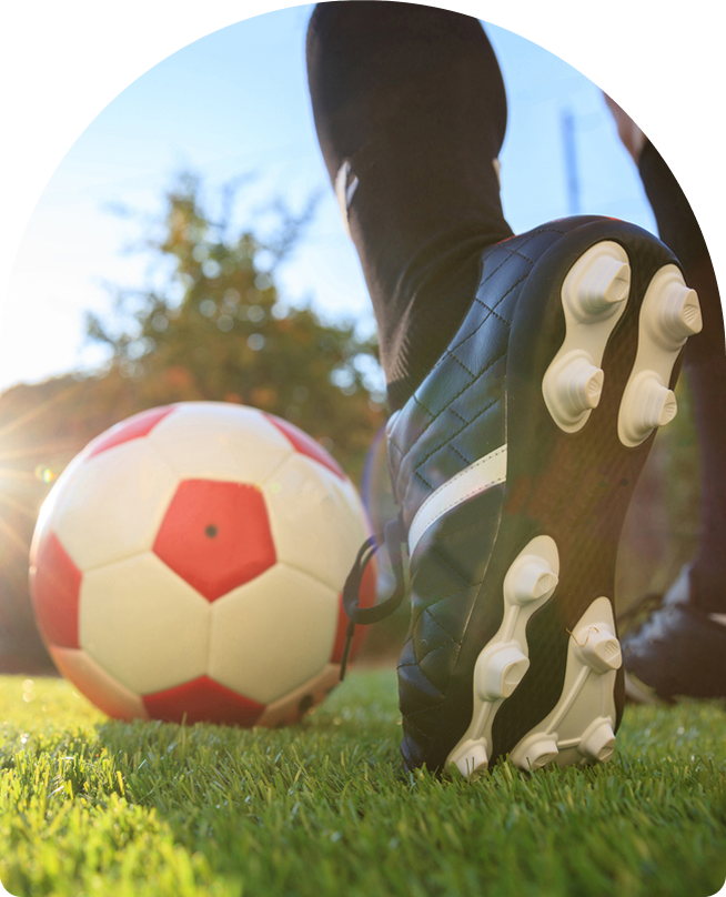 Close-up of soccer cleat next to a red-and-white soccer ball on grass, emphasizing athletic readiness for young female players in a strength training program.