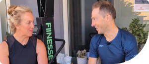Two individuals engaged in a conversation about wellness and fitness, with a fitness equipment backdrop, emphasizing community and personal training insights.