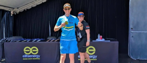 Two smiling individuals posing together at an event, wearing athletic attire, with a branded table displaying energy products in the background, highlighting community engagement in wellness and fitness.