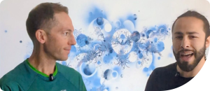 Two men engaged in conversation against a colorful abstract background, discussing wellness and health insights related to the Wellness on Shore community.