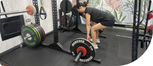 Woman performing a deadlift in a gym setting, showcasing strength training and fitness recovery related to wellness and personal training.