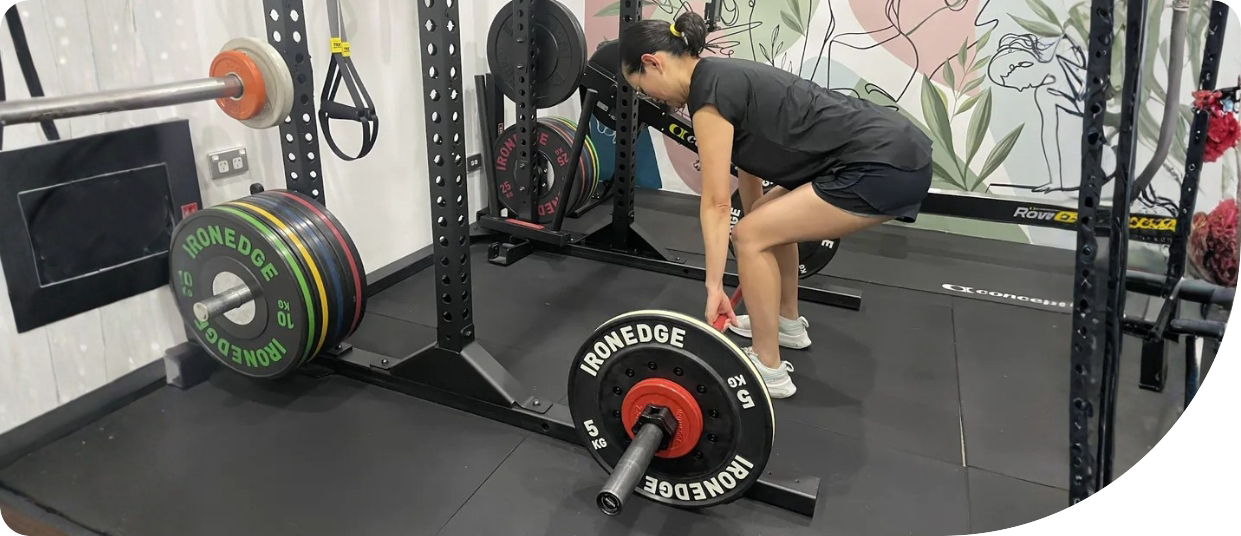 Woman performing a deadlift in a gym, focusing on strength training with weight plates labeled "IRONEDGE," emphasizing personal fitness and wellness journey.