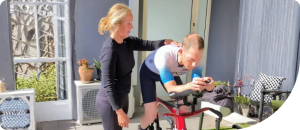 Personal trainer assisting a cyclist on a stationary bike, focusing on strength and technique for improved performance in the World Championships.