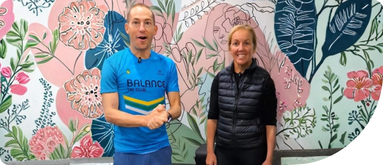 Ben Taylor and Lisa at Wellness On Shore, smiling in front of a floral mural, discussing proactive training for the World Triathlon Championships.