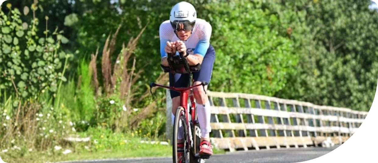 Athlete in triathlon gear riding a red bicycle, focused on training for the 2025 World Triathlon Championships in Wollongong, surrounded by greenery.