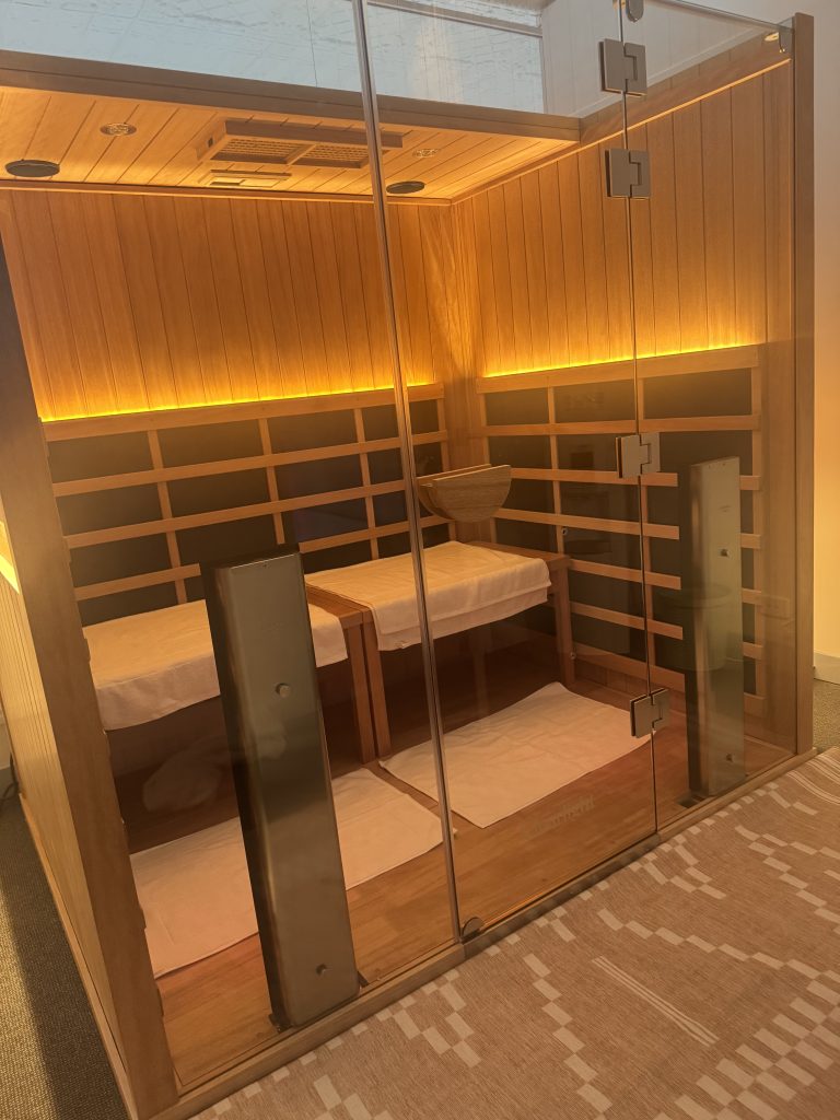 Wellness on Shore treatment room featuring a wooden sauna with soft lighting and two massage tables, inviting relaxation and wellness experiences.
