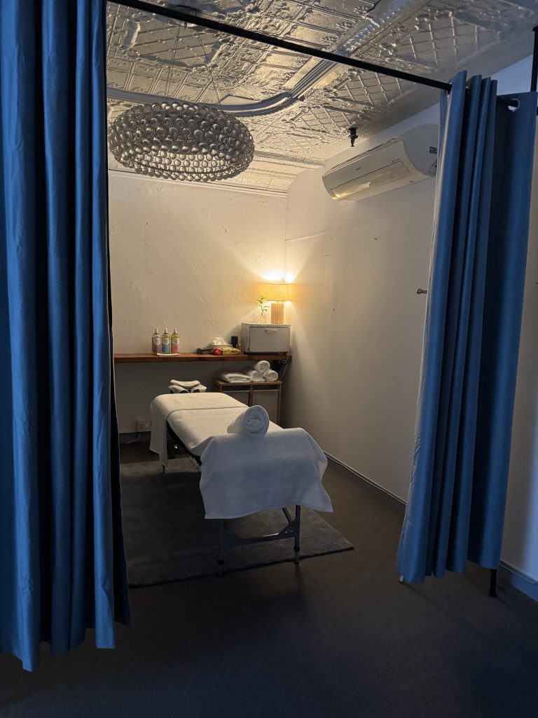 Massage treatment room at Wellness on Shore featuring a massage table, towels, soothing lighting, and decorative elements.