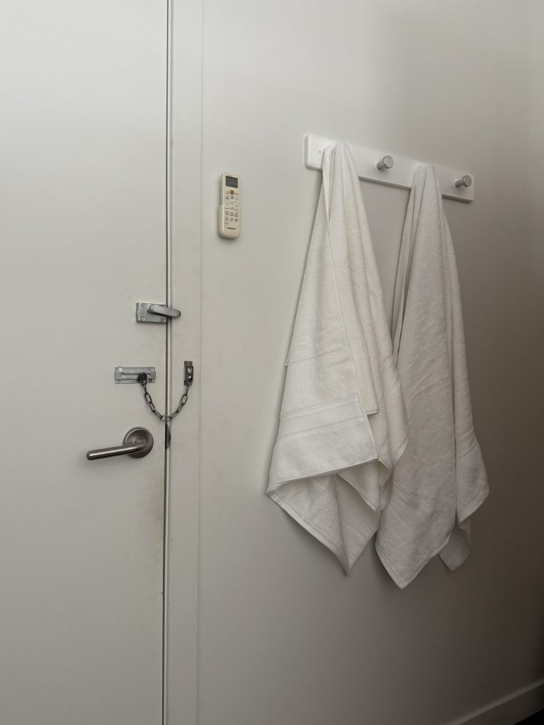 White towels hanging on a hook next to a secured door with a chain lock and an intercom, representing the treatment room environment at Wellness on Shore.