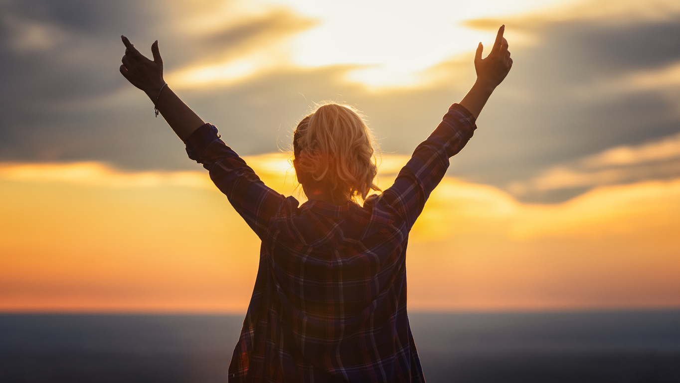 Person with arms raised in celebration against a sunset backdrop, symbolizing relaxation and rejuvenation, related to massage therapy benefits.