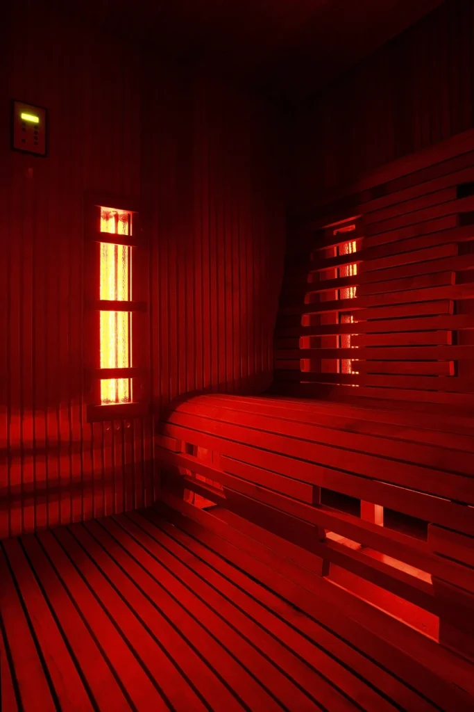 Infrared sauna interior with glowing red lights, wooden benches, and heater panels, illustrating the environment for targeted heat therapy and relaxation.