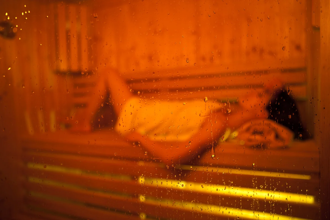 Person relaxing in an infrared sauna, surrounded by a warm, orange glow and condensation on the glass, illustrating the benefits of sauna therapy for detoxification and lymphatic health.