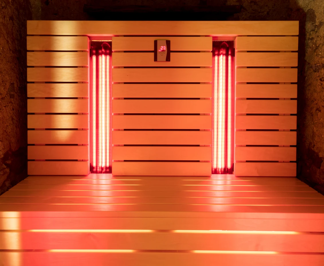 Infrared sauna interior with glowing red lights and wooden slats, showcasing heat therapy environment for recovery and wellness.