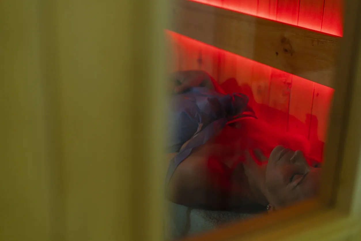 Woman relaxing in an infrared sauna with red lighting, promoting muscle recovery and wellness.
