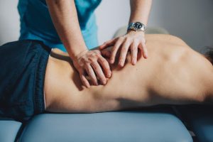 Remedial massage therapy session focusing on muscle recovery, with therapist's hands applying pressure on patient's back.